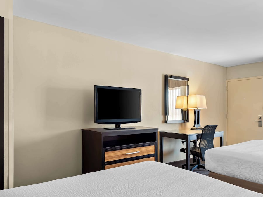 A hotel room with two beds, a TV on a wooden cabinet, a desk with a chair, and a lamp.