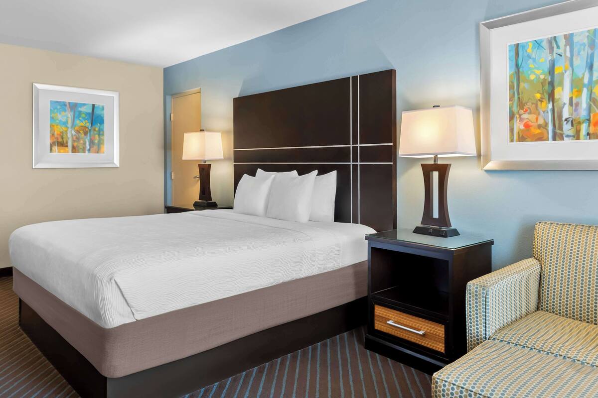 A hotel room with a large bed, two bedside tables with lamps, a chair, and two framed artworks on the walls.