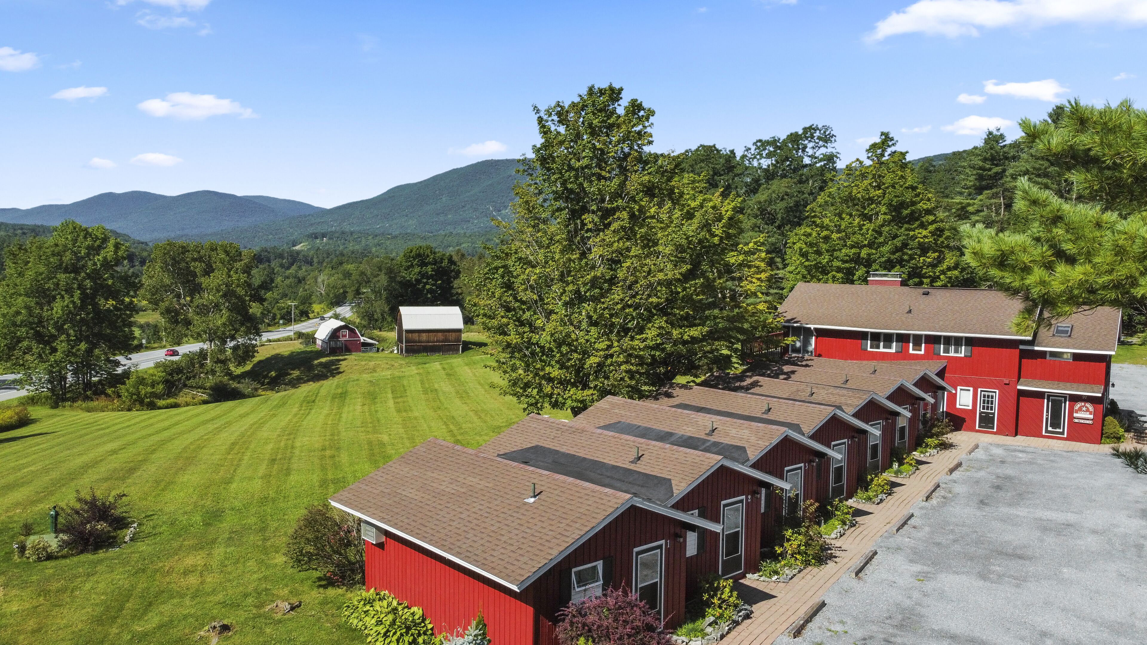 A row of red cabins with a grassy lawn and a barn in the background.
