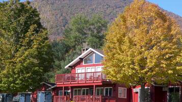 A two-story red building with a balcony, surrounded by trees with autumn foliage, set against a backdrop of a hill.