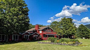 A large, red, two-story building with a balcony, surrounded by lush greenery and a clear blue sky. - North Shire Lodge (Manchester Center)
