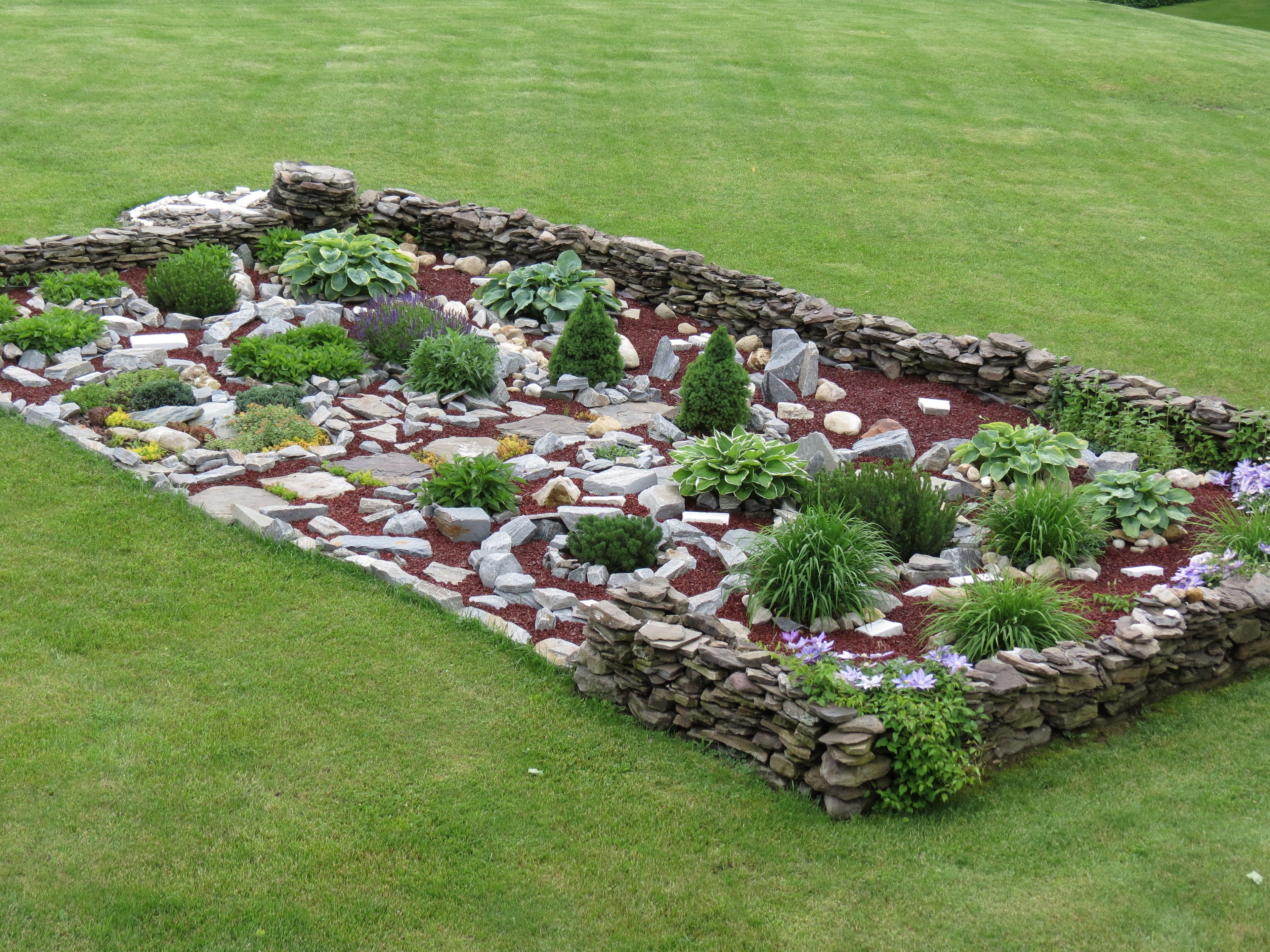 Un jardín con borde de piedra, distintas plantas y césped bien cuidado.