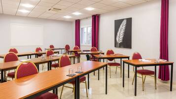 Un salón de conferencias con varias mesas y sillas, un ventanal con cortinas y una obra de arte con plumas en la pared.