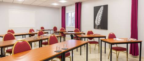 Un salón de conferencias con varias mesas y sillas, un ventanal con cortinas y una obra de arte con plumas en la pared.