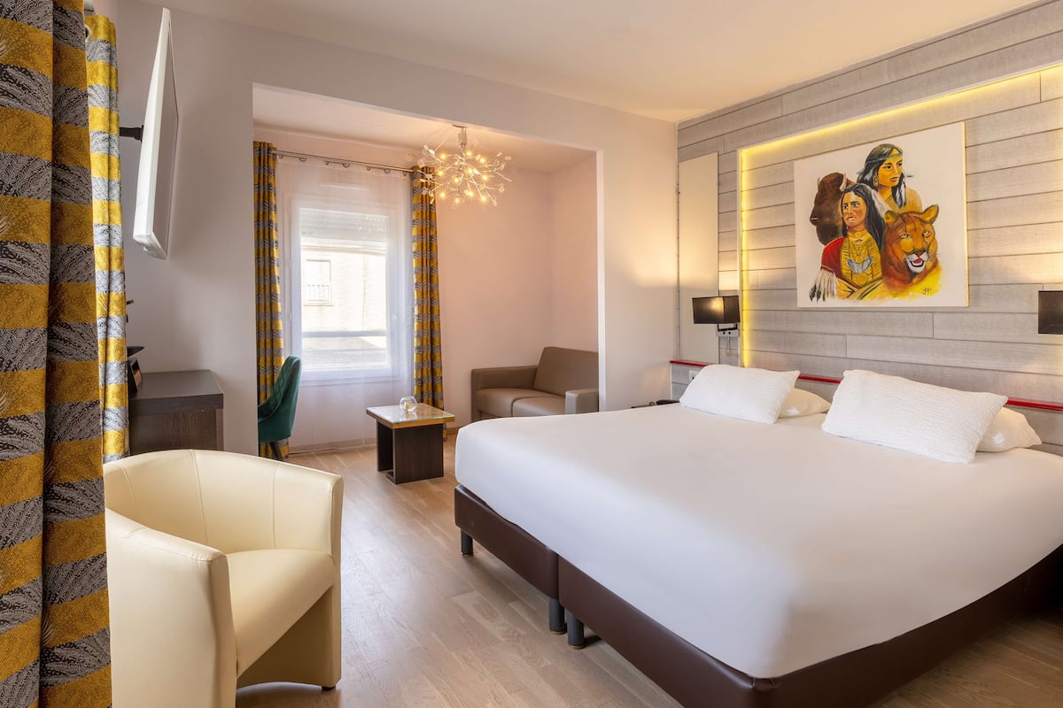 A hotel room with a large bed, a sofa, a small table, and a painting on the wall.