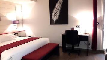 A hotel room with a bed, desk, and a feather artwork on the wall.