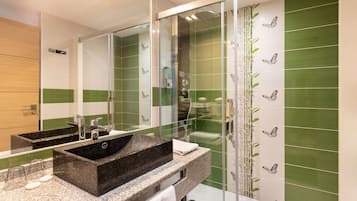 A modern bathroom with a large mirror, a black sink, and green-tiled walls.