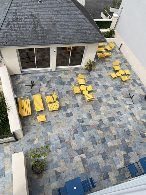A rooftop patio with yellow chairs and tables, stone flooring, and a view of the building's interior.