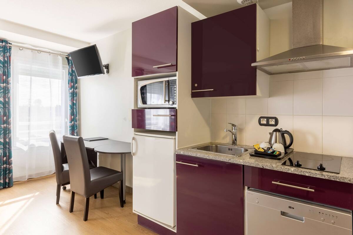 A compact kitchen with a microwave, stove, and dishwasher. There is a dining area with a table and chairs.