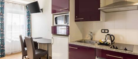 A compact kitchen with a microwave, stove, and dishwasher. There is a dining area with a table and chairs.