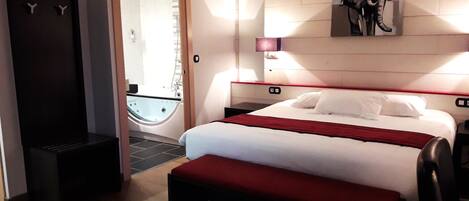 A hotel room with a bed, a bench, a shower, and a painting on the wall.