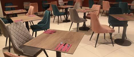 A dining area with multiple tables and chairs, some with pink cushions.