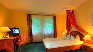 Ein Hotelzimmer mit einem Bett, einem Schreibtisch mit Fernseher, einem Sessel und einem Fenster mit Vorhängen.