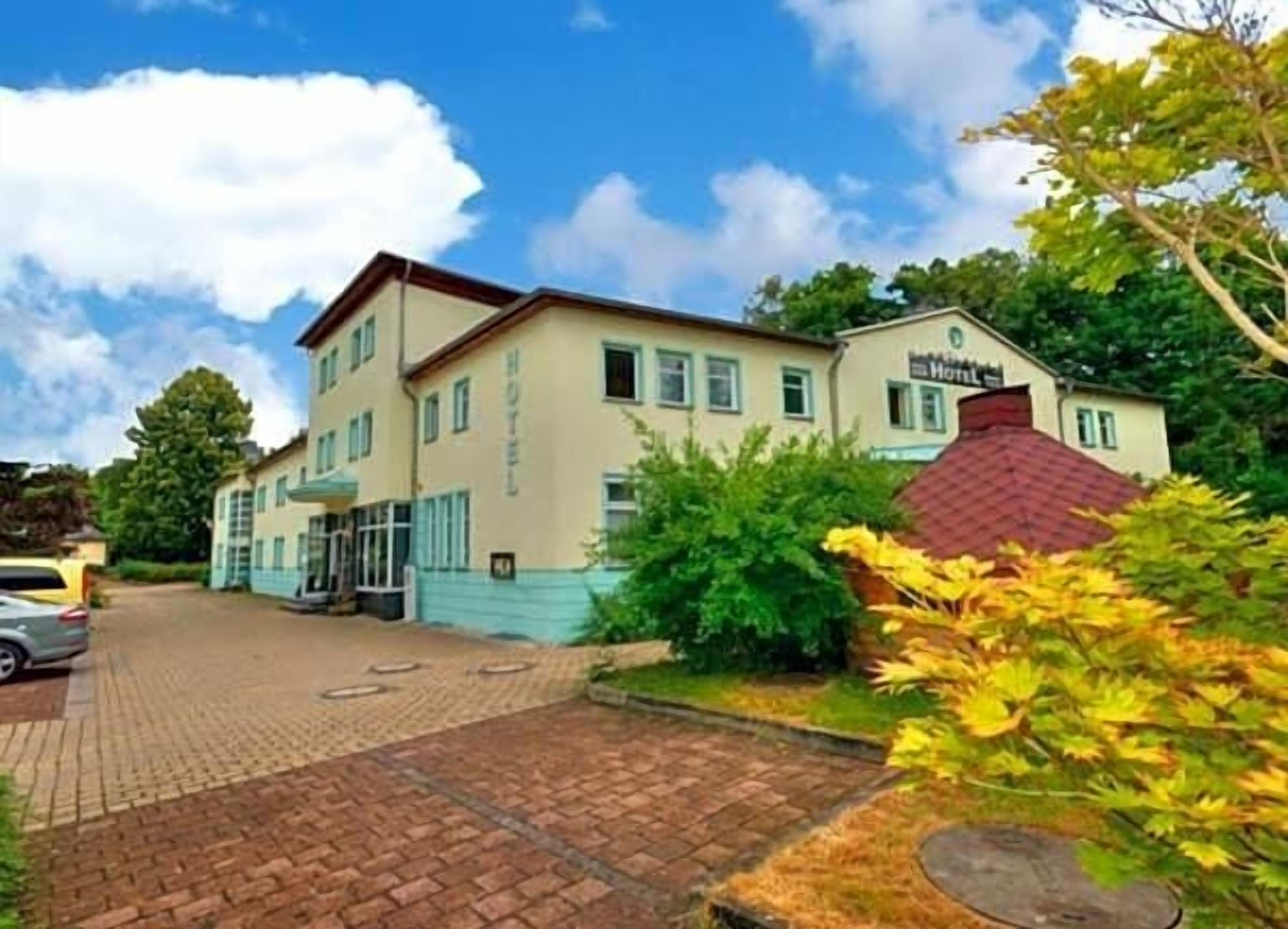 Ein Hotel mit Kopfsteinpflasterauffahrt und einem Gartenbereich mit gelbem Laub.