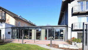 A modern building with a glass facade, outdoor seating area, and a clear sky. - WESTSIDE Hotel Garni (Munich)