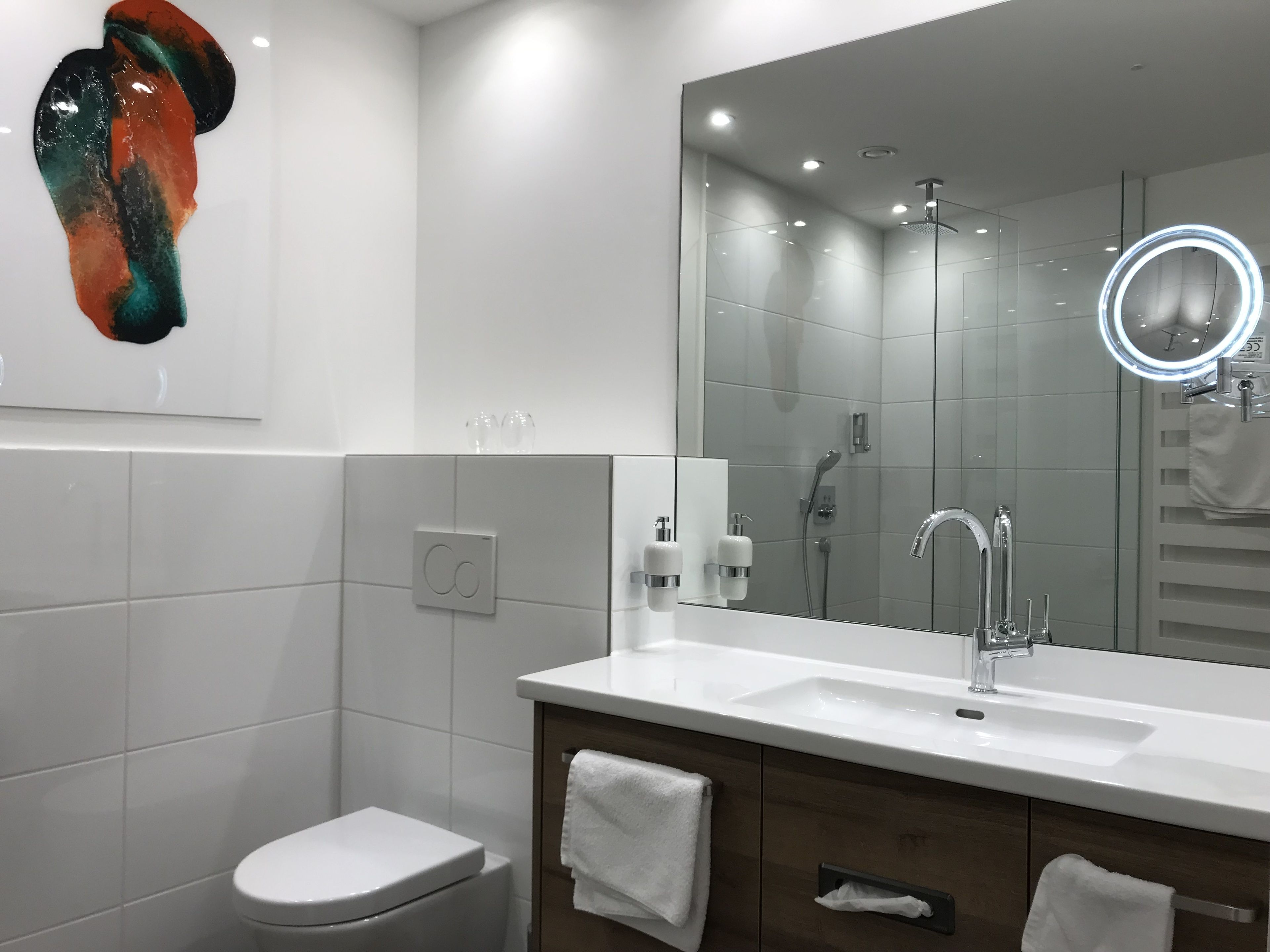 Un baño moderno con lavamanos blanco, un espejo grande y una ducha.