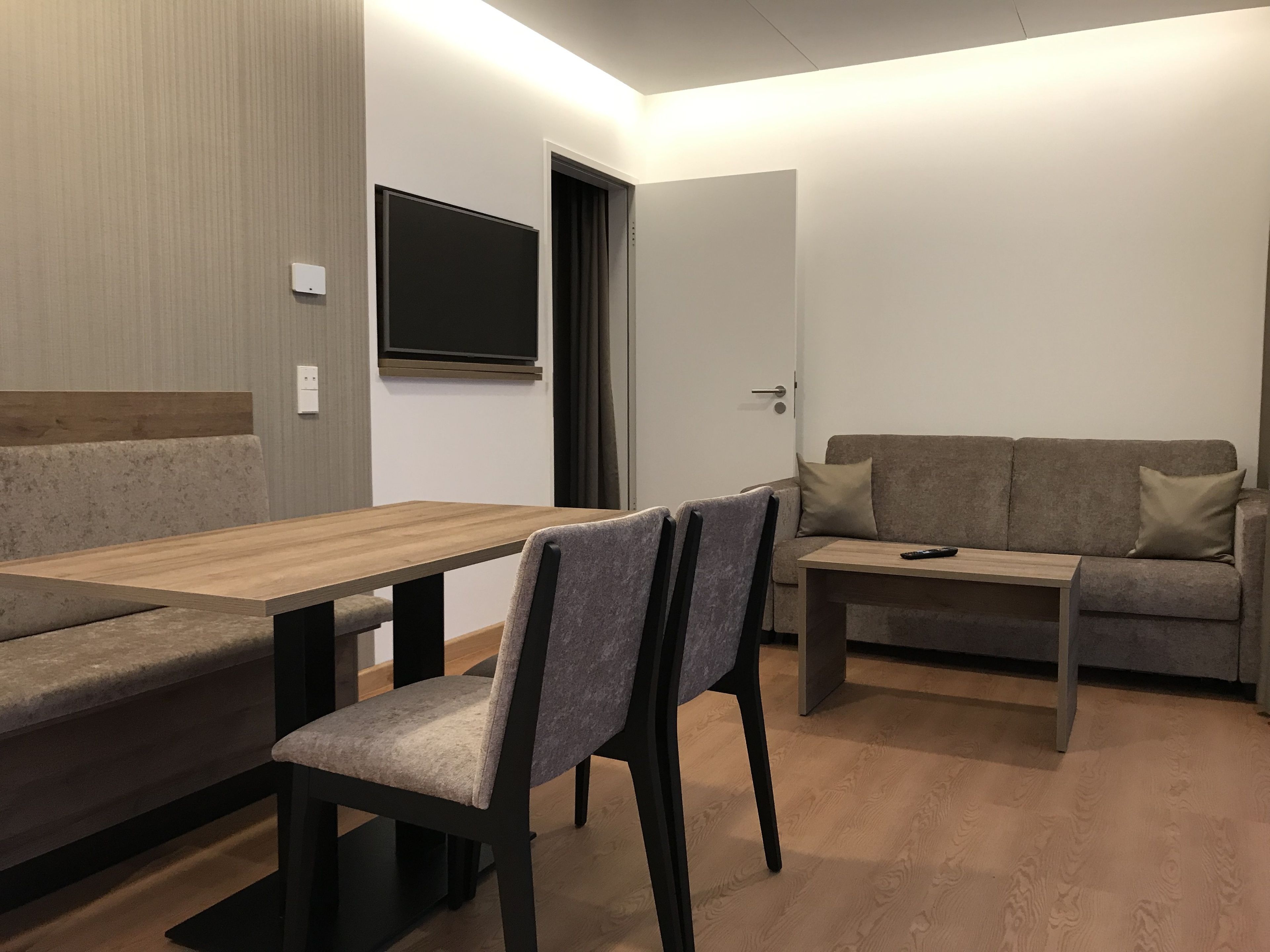 Una sala de estar moderna con una mesa de comedor de madera, un sofá y un televisor montado en la pared.