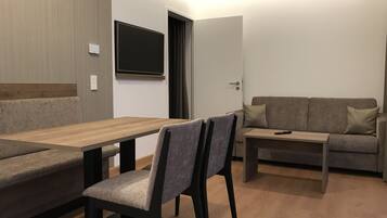 Una sala de estar moderna con una mesa de comedor de madera, un sofá y un televisor montado en la pared.