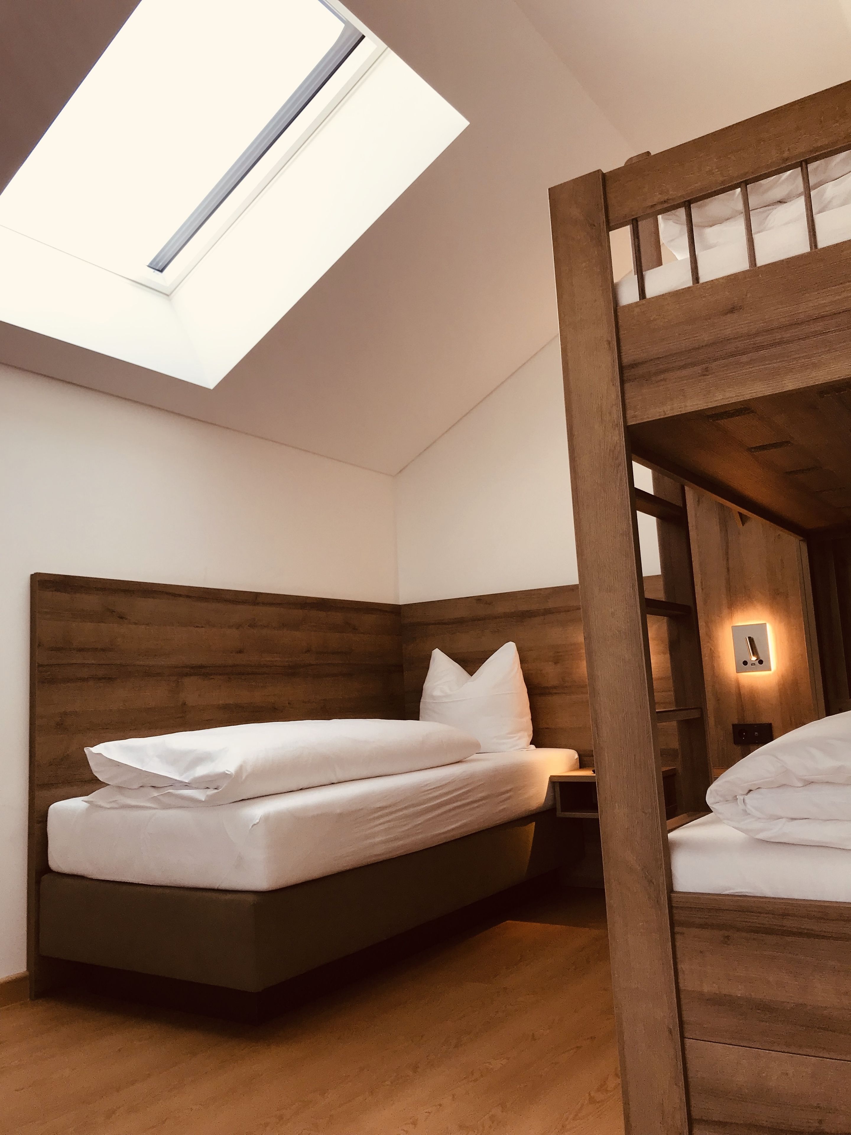 A bedroom with a bunk bed, a skylight, and a bedside table with a lamp.