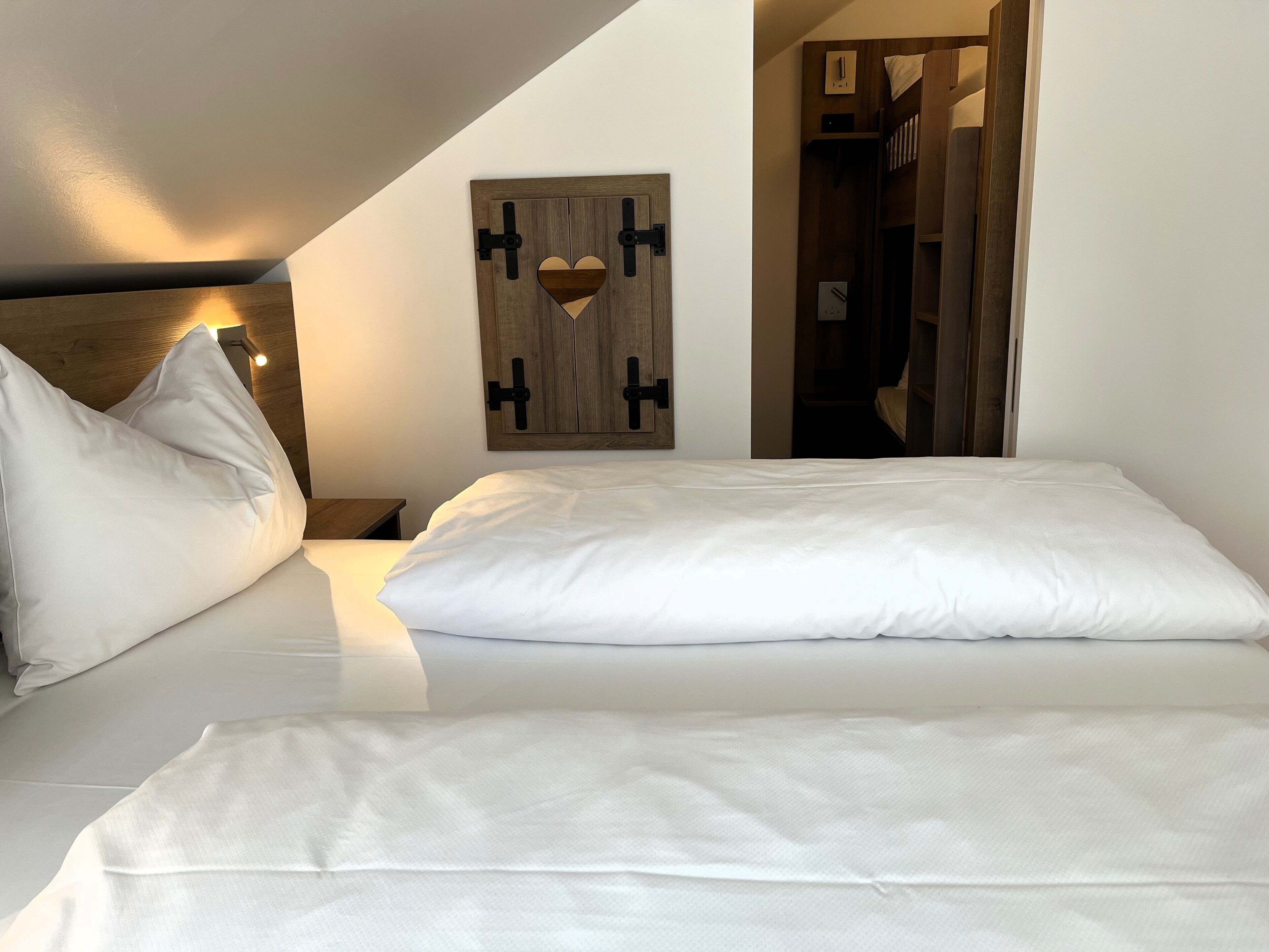 Un dormitorio con cama, almohadas, cabecera de madera, decoración en forma de corazón en la pared y mesita de noche.