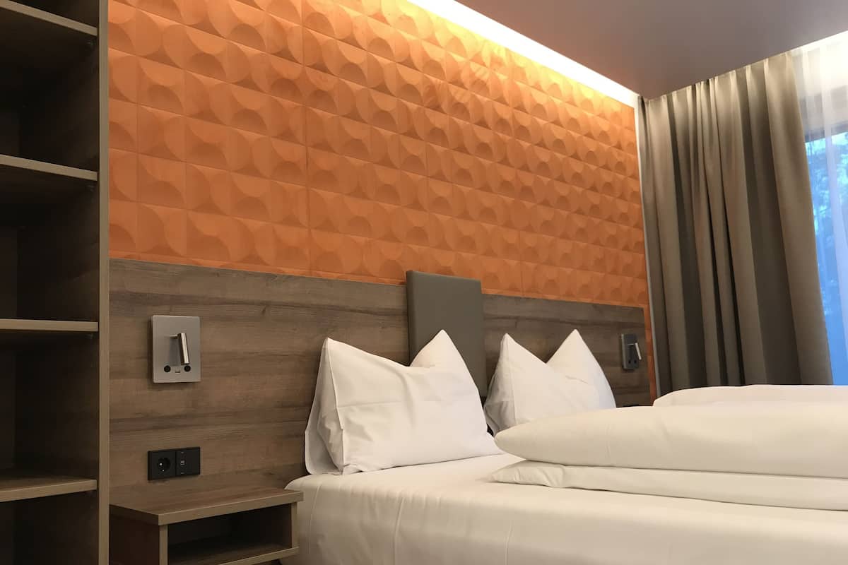 Une chambre dâhĂŽtel avec une tĂȘte de lit en bois, une Ă©tagĂšre intĂ©grĂ©e et un lit avec du linge de lit blanc.