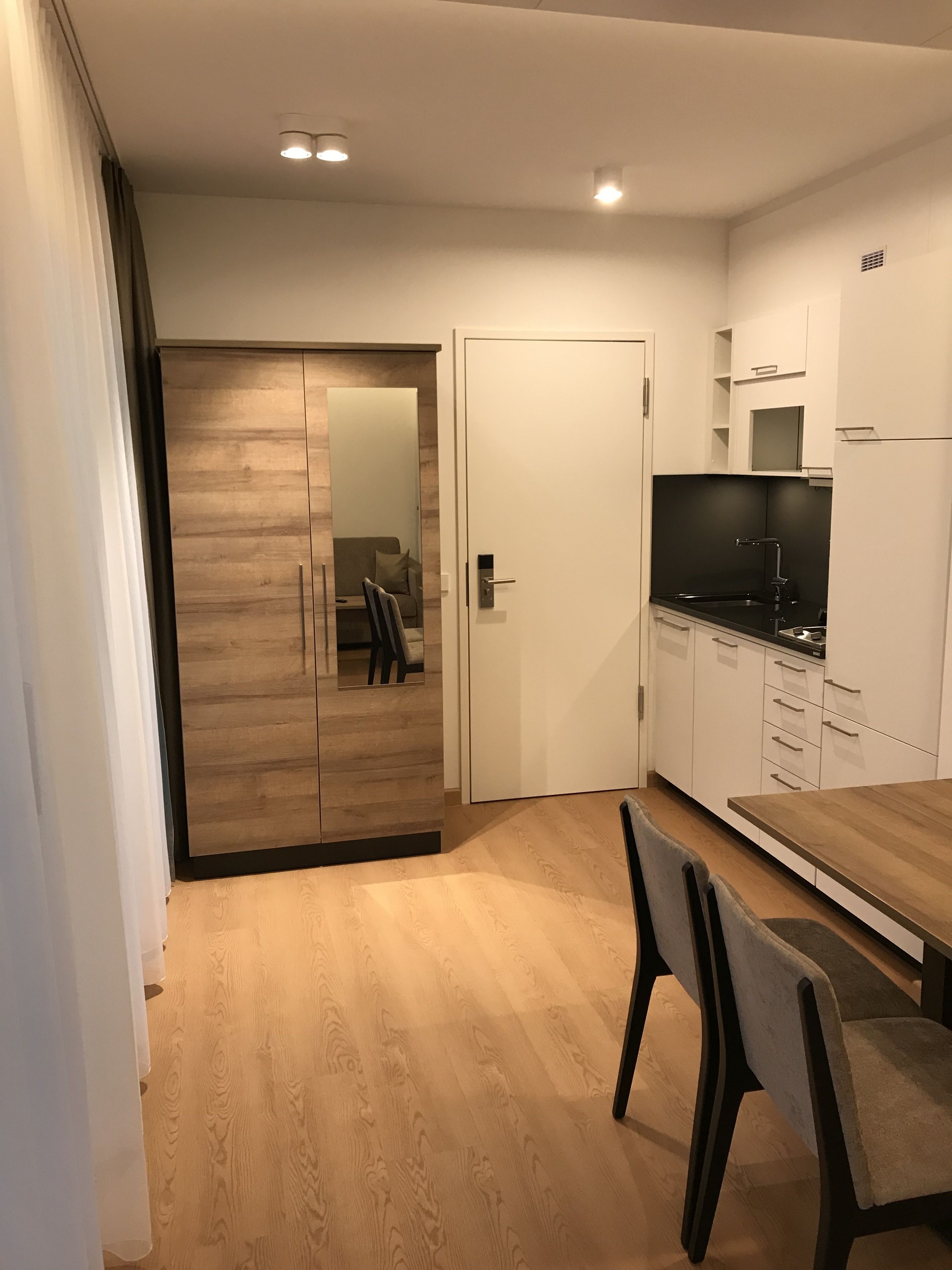 A modern kitchen with white cabinets, a black countertop, and a wooden dining table.
