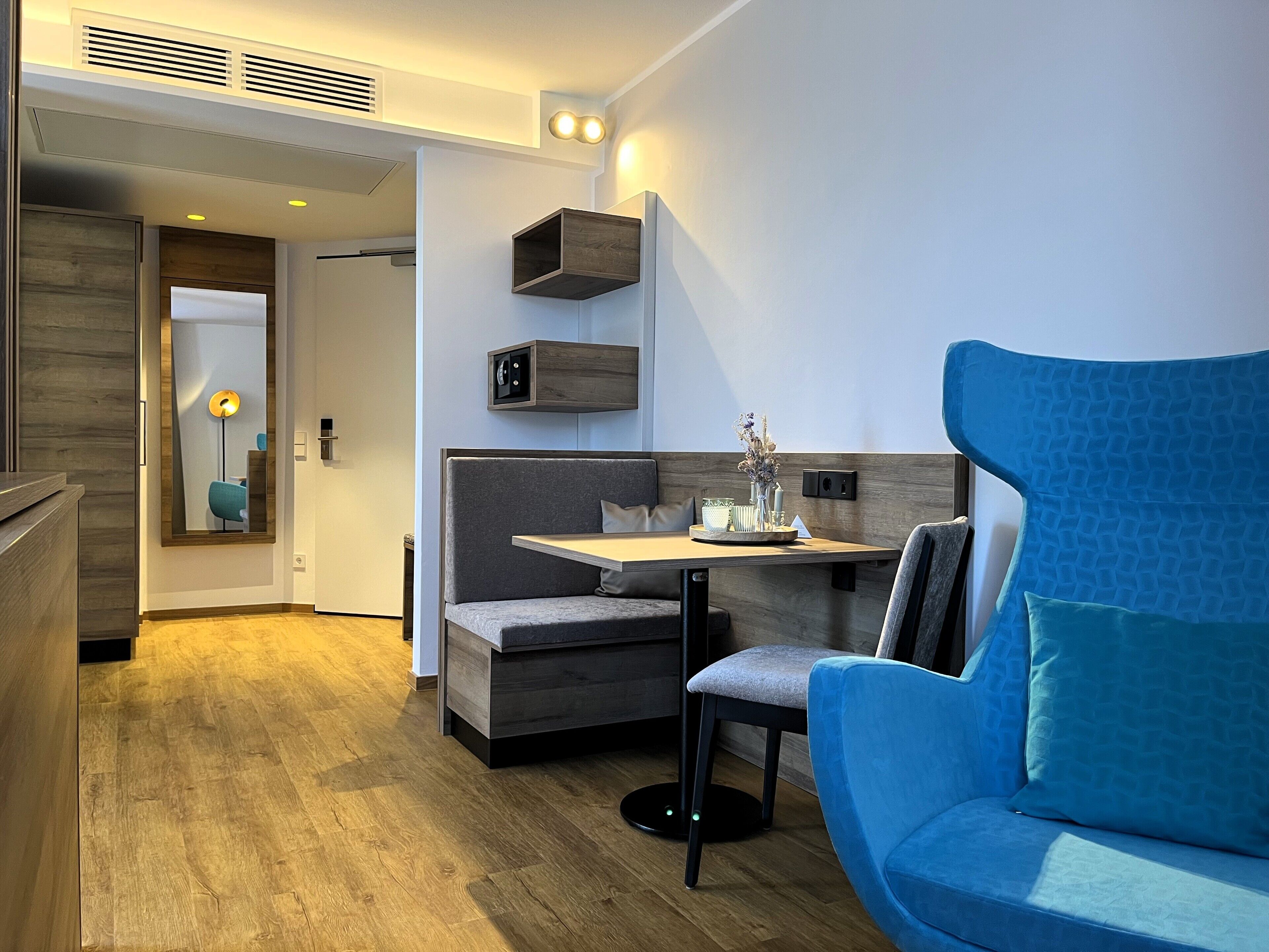 A compact, modern room with a built-in bench, a small table, and a blue sofa.