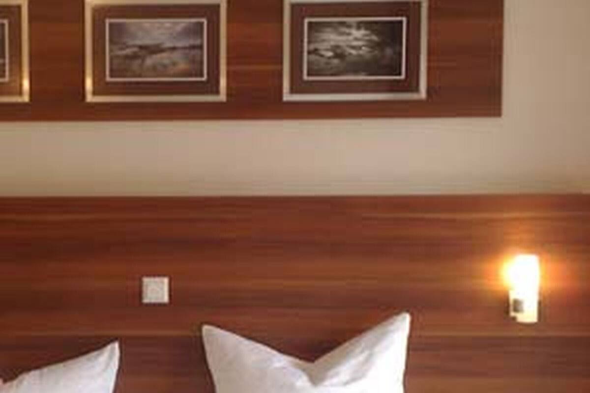 A hotel room with a wooden headboard, two beds with white linens, and three framed pictures on the wall.