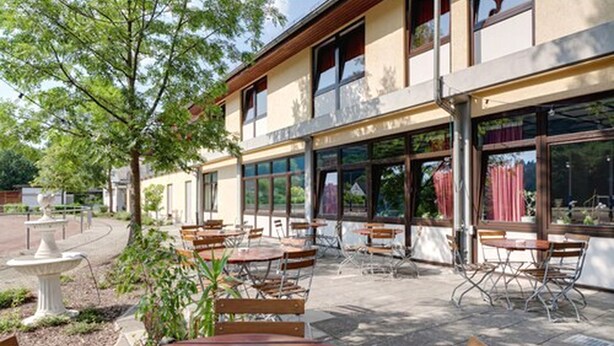 Un patio al aire libre con mesas, sillas, una fuente y un edificio con grandes ventanales.