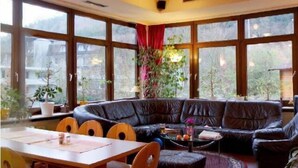 Una sala de estar acogedora con un sofá de cuero negro curvo, una mesa de comedor con sillas y ventanas grandes con cortinas.