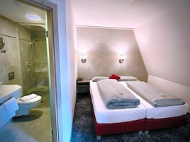 Quarto com chuveiro, sanita e cama de duas almofadas.