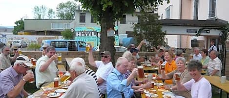 Un grupo de personas sentadas en mesas al aire libre, disfrutando de bebidas y comida en un ambiente relajado.