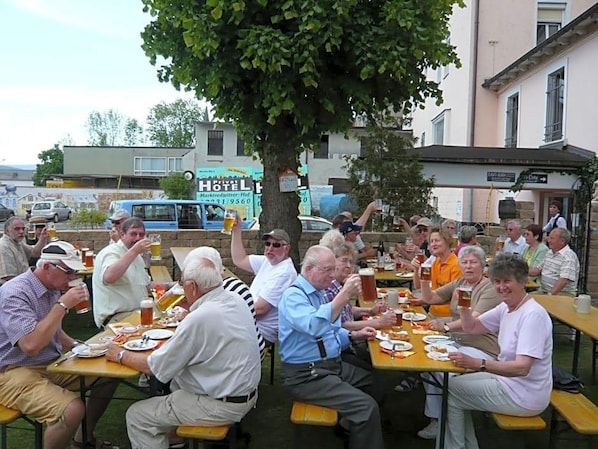A group of people seated at outdoor tables, enjoying drinks and food in a casual outdoor setting.