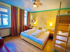 A hotel room with a bed, a desk, a chair, a ladder, and a window with curtains.