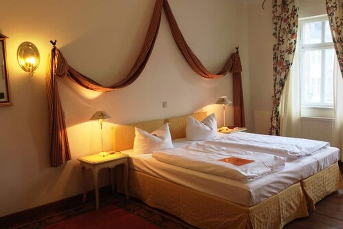 A bedroom with a bed, bedside tables, a nightstand, a hanging curtain, and a window with floral curtains.