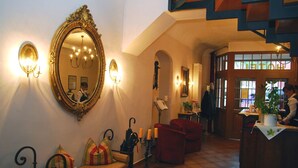 A hotel lobby with a large ornate mirror, a red sofa, a bench, and a reception desk. - Hotel Adler (Rudolstadt)