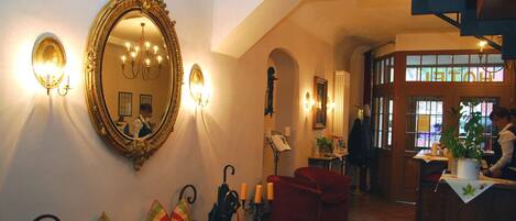 A hotel lobby with a large ornate mirror, a red sofa, a bench, and a reception desk.