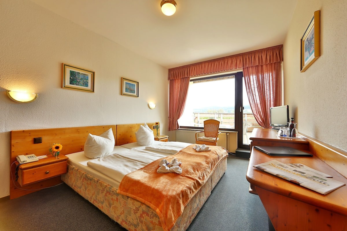 A hotel room with a large bed, a desk, a chair, and a window with curtains.