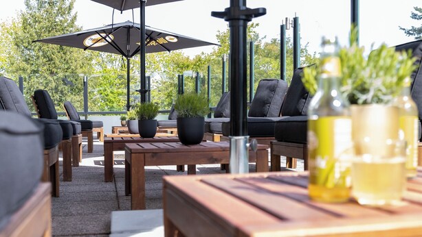 Un espace extérieur aménagé avec des tables et des chaises en bois, des plantes en pot et des parasols.