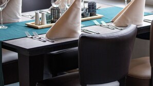 Une table à manger dressée avec des serviettes blanches, des couverts en argent et de la verrerie, et une vue sur la verdure à travers une fenêtre.