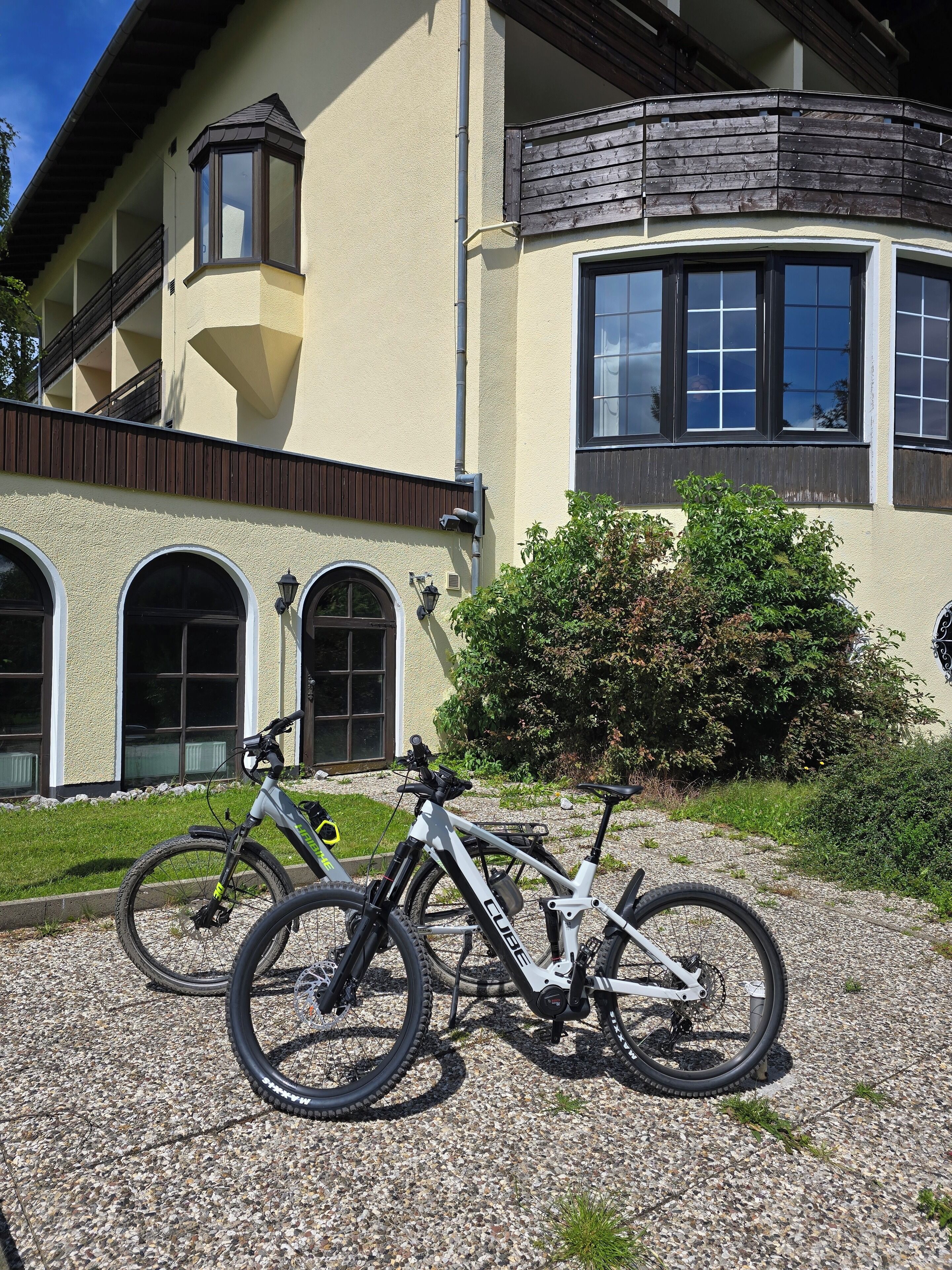 A building with a beige exterior, a balcony with wooden railings, and a gravel driveway.