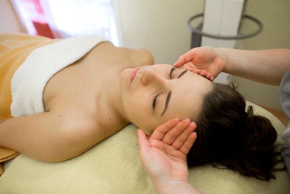 A person lying on a bed with a towel wrapped around their shoulders, receiving a facial treatment.