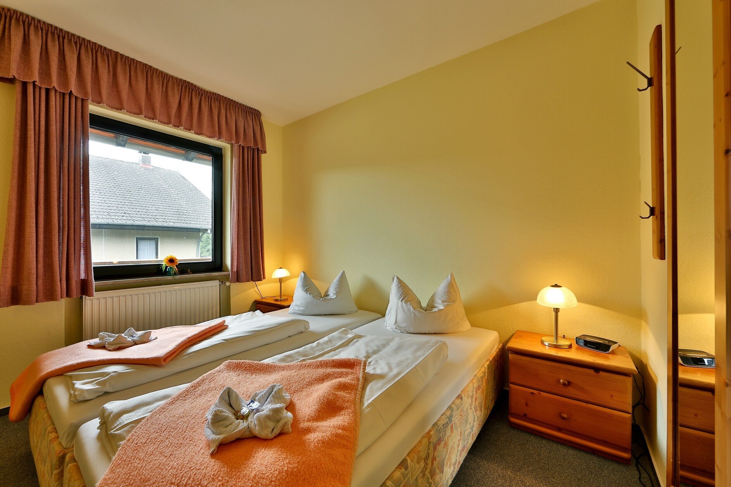Habitación de hotel con dos camas, una ventana con cortinas, una lámpara de noche y una mesita de noche de madera.