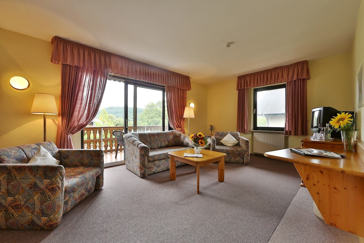 A living room with patterned sofas, a wooden coffee table, and a TV on a wooden stand.