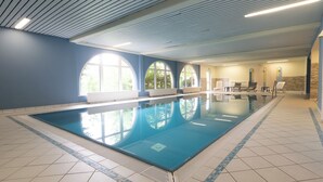Une piscine intérieure dotée d’un sol carrelé, de grandes fenêtres en arc de cercle et d’un plafond équipé de luminaires linéaires.
