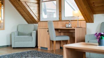 A cozy attic room with a wooden desk, two chairs, and a large window providing natural light.