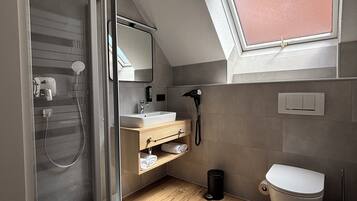 A modern bathroom with a glass shower enclosure, a wooden vanity, a white toilet, and a skylight.