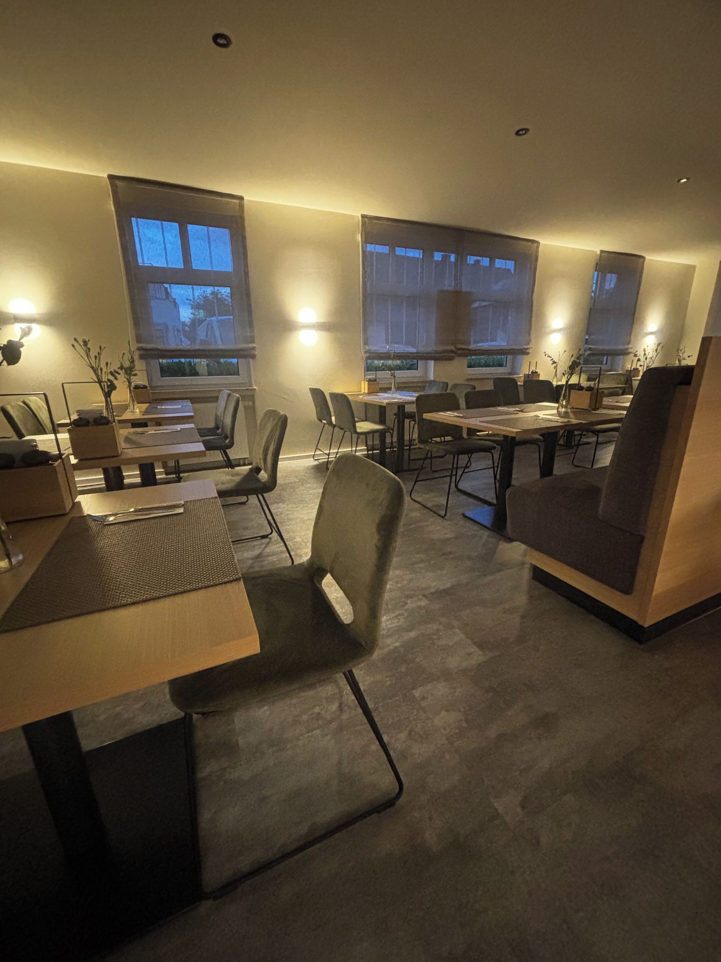 Un comedor moderno con mesas y sillas, ventanas amplias e iluminación ambiental.