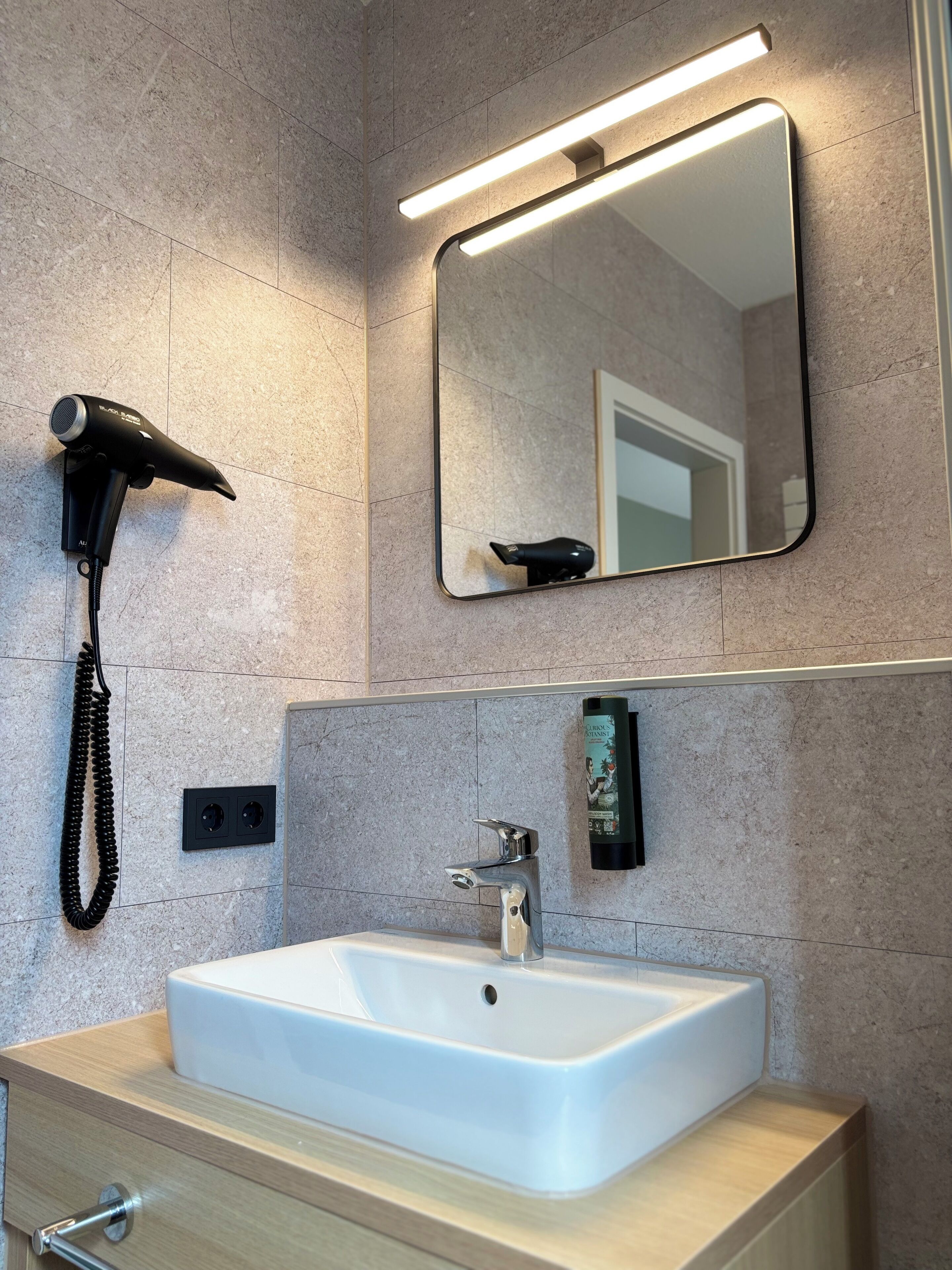 A bathroom with a white sink, a mirror, a hairdryer, and a wall-mounted light fixture.