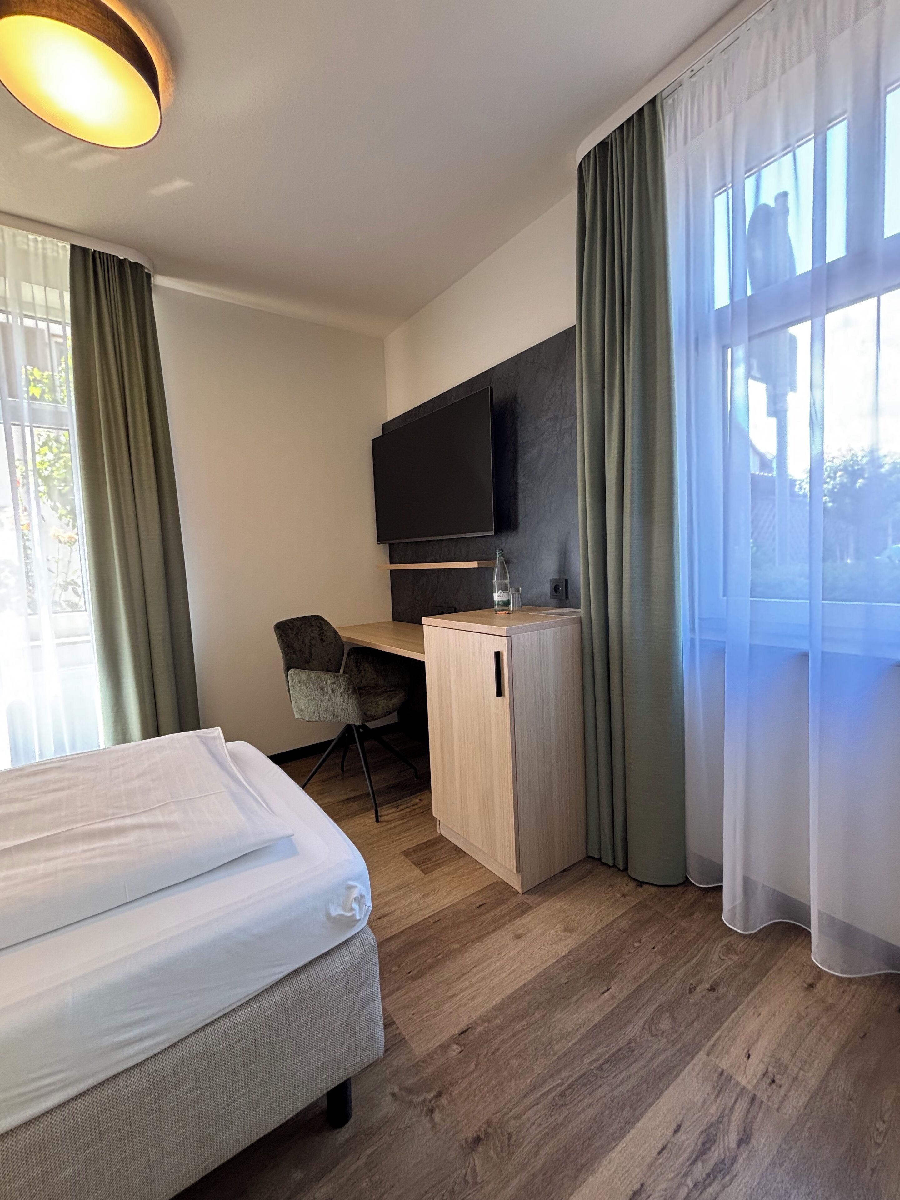 A hotel room with a bed, a desk with a TV, and a window with curtains.